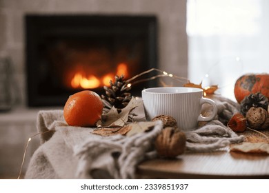 Cozy autumn. Warm cup of tea, pumpkins, autumn leaves, cones, cozy scarf on rustic wooden table on background of fireplace in farmhouse. Comfort fall in rural home. Happy Thanksgiving - Powered by Shutterstock