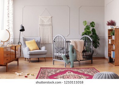 Cozy baby room with comfortable armchair with yellow pillow and grey wooden crib, real photo