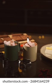 Cozy baking setup features mugs with marshmallows, cookie cutters on dark wooden table, plate in background. Warm, festive mood ideal for holiday cooking, winter treats, family-friendly kitchen moment