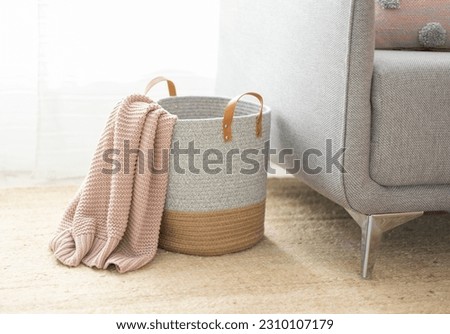 A cozy basket filled with a warm pink blanket, placed next to a comfortable couch in a home interior setting