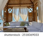 Cozy beach cabana with white curtains overlooking the ocean at sunset on a serene evening