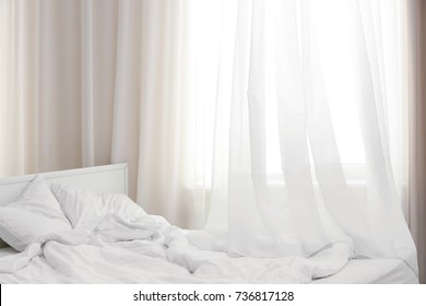 Cozy bed near window with beautiful curtains in room
