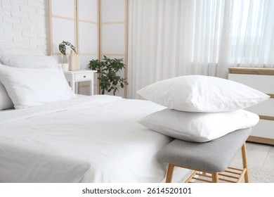 Cozy bed with white blanket and stack of soft pillows on bedside bench in stylish bedroom, closeup