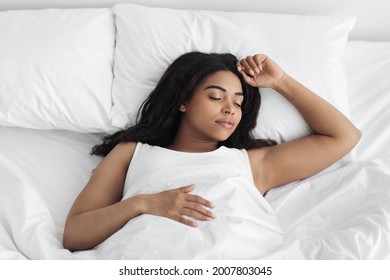 Cozy Bedtime. Young African American Woman Sleeping In White Bed At Home, Copy Space, Top View. Peaceful Black Lady Having Nap, Resting In Cozy Bedroom. Healthy Sleeping Concept