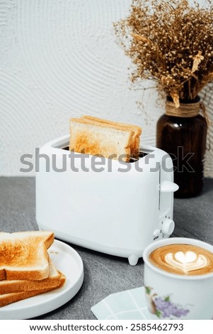 A cozy breakfast setup featuring a white toaster with golden-brown toast, a cup of coffee, and a plate of toasted bread, set against a stylish kitchen backdrop with warm decor