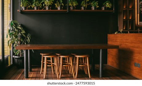 Cozy cafe setting with a long wooden table and six matching stools on a wooden floor. A large potted plant in the corner adds a touch of greenery against the dark wall, creating a warm ambiance. - Powered by Shutterstock