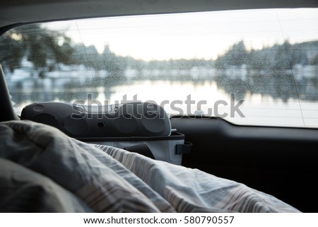 Cozy car backseat on cold snowy winter day with striped quilt and boom box with view of lake shore put of rear window 
