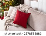 Cozy Christmas Ambiance, A Neutral-Toned Sofa Adorned with Textured Cushions, Rich Red Accent Pillow, Chunky Knit Throw, Set Against a Glittering Christmas Tree Illuminated by Golden Lights, Close Up