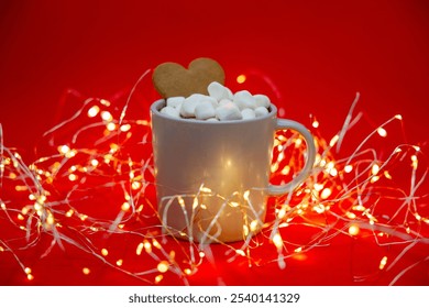 A cozy Christmas scene: a cup of hot cocoa with marshmallows and a heart-shaped gingerbread cookie on a red background, illuminated by warm string lights for a festive, holiday atmosphere. - Powered by Shutterstock