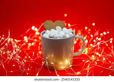 A cozy Christmas scene: a cup of hot cocoa with marshmallows and a heart-shaped gingerbread cookie on a red background, illuminated by warm string lights for a festive, holiday atmosphere. - Powered by Shutterstock