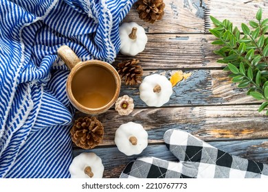 Cozy coffee and blue striped blanket flatlay background, with a plaid oven mitt, and white pumpkins and pine cones - Powered by Shutterstock