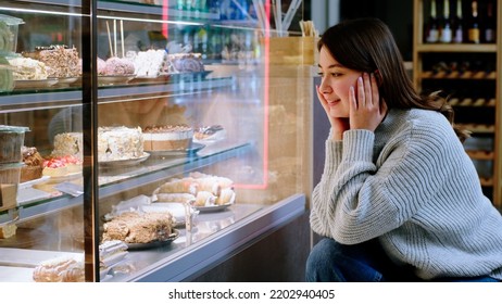 At the cozy coffee shop happy lady very hungry looking at the showcase fridge to choose her favourite dessert - Powered by Shutterstock