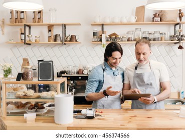 Cozy coffeehouse. Merry and positive two handsome male cafe workers using digital tablet at work during the break - Powered by Shutterstock