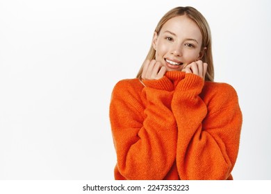 Cozy and comfort. Beautiful tender woman, getting comfortable and warm in her red stylish sweater, enjoy clothes quality, white background - Powered by Shutterstock