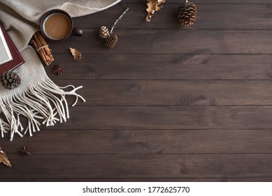 Cozy composition with soft plaid and cup of coffee. Seasonal autumn or winter coziness with warm blanket, coffee, books and pine cones. Cozy home and hygge concept on wooden background, copy space.