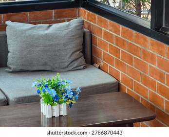 Cozy corner featuring gray sofa against red brick wall behind dark wooden table holding small blue flower vase creating peaceful relaxing atmosphere for quiet indoor living space