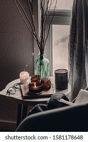 Cozy corner in the living room. Cozy warm blanket. Winter time. Candles on the table. Scandinavian interior decor. Cold winter time. Grey chair, throw blanket. Reading a book. Warm and cozy home