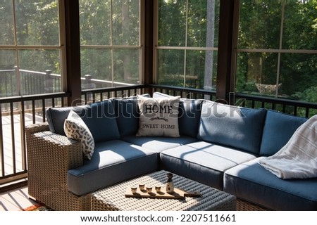 A cozy corner of an outdoor living space with modern porch windows, patio furniture, cushions and pillows. Ceramic sake set and cups on coffee table, woods in the background.