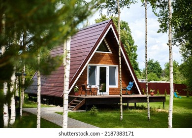 Cozy cottage house with open terrace and large sloping roof. Modern building in triangle shape surrounded by lush greenery and trees in countryside - Powered by Shutterstock