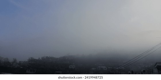 Cozy cottages perch amidst the clouds, their rooftops adorned with a fresh layer of snow, while the tentative rays of the rising sun pierce through the mist, casting an ethereal glow on the wintry sce