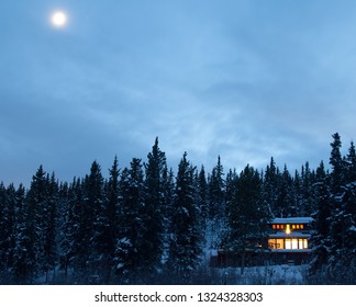 Cozy Country Living Home Warmly Illuminated Isolated In Boreal Forest Taiga Moon-lit Frozen Winter Landscape Of Remote Yukon Territory, YT, Canada