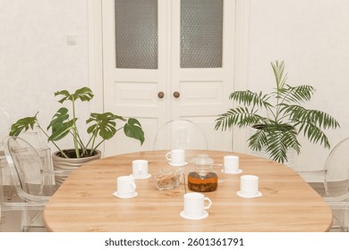 Cozy dining setting featuring a round wooden table surrounded by transparent chairs, complemented by lush green potted plants, creating a warm and inviting interior atmosphere. - Powered by Shutterstock - Get 15% off with code: PIKWIZARD15