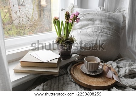 Cozy Easter, spring still life scene. Cup of coffee, books and blank greeting card on windowsill. Vintage feminine styled photo. Moody floral composition. Potted pink hyacinth flowers. Linen plaid.