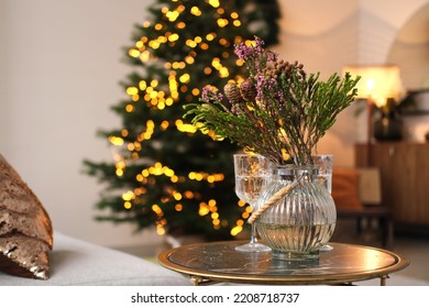 Cozy evening home interior - sofa, table, vase with a bouquet of Christmas tree branches against the background of Christmas lights. Horizontal photo