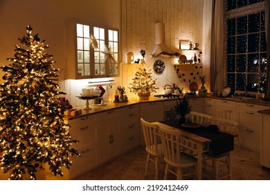 Cozy evening kitchen decorated for Christmas. Christmas tree with lots of garland lights in scandinavian kitchen with dining table. Christmas interior. Christmas Eve. Holiday dinner atmosphere. - Powered by Shutterstock