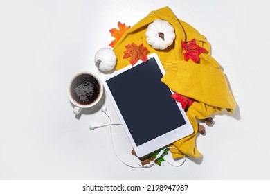 Cozy Fall Background With Coffee Cup, Tablet Notebook, Ear-pods, White, Orange Pumpkins, Autumn Leaves Decor On White Home Office Table Background. Autumn Still Life Composition Flatlay