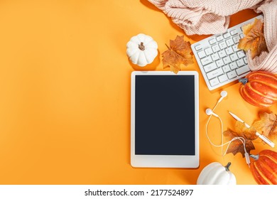 Cozy Fall Background With Tablet, Ear-pods, White, Orange Pumpkins, Autumn Leaves Decor On High-colored Orange Background. Autumn Still Life Composition. 