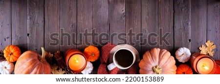 Cozy fall bottom border with pumpkins, sweaters, candles and coffee. Top view over a dark wood banner background.