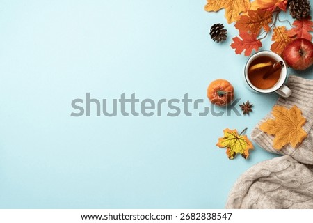 Cozy fall flat lay background. Knitted sweater, falling leaves and crafted candle on blue background.