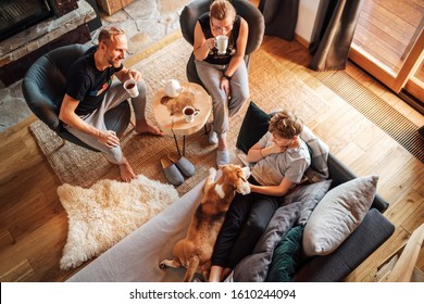 Gemütlicher Familientee. Vater, Mutter und Sohn im Wohnzimmer. Junge, die in einem bequemen Sofa liegen und ihren Adlerhund streicheln und lächeln. Bild von friedlichen Familienmomenten.