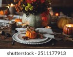 Cozy festive holiday table decor for home family Thanksgiving dinner. Traditional event, elegant natural decoration. Wooden rustic table, countryside style. Burning candles, floral centrepiece pumpkin