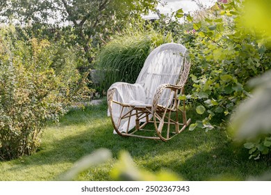 Cozy garden corner with wicker rocking chair. Calm outdoor seating for relaxation. Garden furniture against the background of lush plants. Garden planning and plant care. Horizontal photo - Powered by Shutterstock