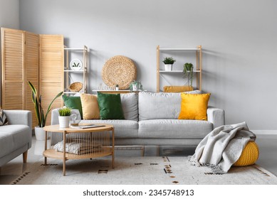 Cozy grey sofa, coffee table and pouf with soft blanket in interior of living room