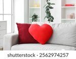 Cozy grey sofa with heart-shaped cushion in living room. Valentine