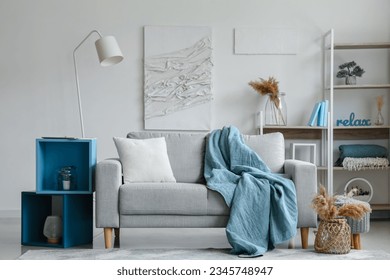 Cozy grey sofa with soft blanket, cushion and stylish shelves in interior of light living room - Shutterstock ID 2345748947