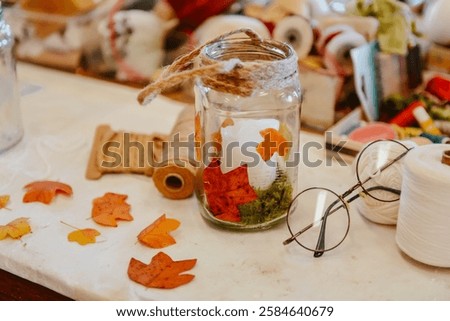 Cozy handmade lanterns crafted from empty jars, adorned with dried autumn leaves and twine, bringing warm and rustic charm to any seasonal decor.