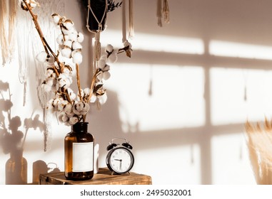 Cozy home decor. Cotton stems in a brown glass vase and a classic black alarm clock on a wooden table. Bohemian and rustic style. Horizontal photo - Powered by Shutterstock