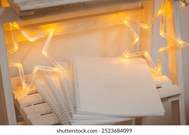 Cozy home decor scene with warm yellow LED lights shaped into a star, illuminating a stack of white spiral notebooks on rustic wooden crates - Powered by Shutterstock