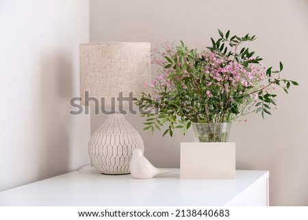 Cozy home desk table with lamp, bunch of spring flowers in vase, greeting card mockup. Hygge, boho style, scandinavian living room