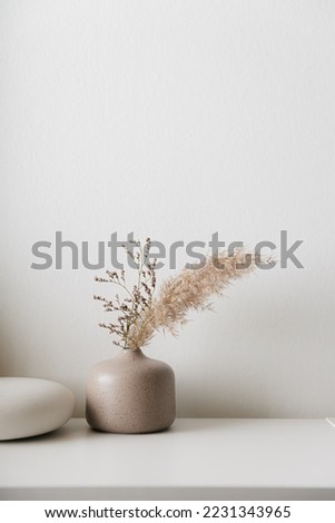 Cozy home interior decor, aromatic candles in glass glowingon white and grey background with natural oil, selective focus of fluffy bunny tail grass, brown jar, lotus flower candle, round matt ceramic