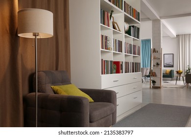 Cozy Home Library Interior With Comfortable Armchair, Floor Lamp And Collection Of Books On Shelves