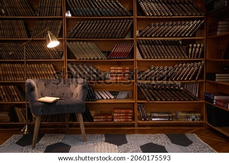 Cozy home library interior with comfortable armchair and collection of vintage books on shelves