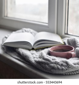 Cozy Home Still Life: Cup Of Hot Coffee And Opened Book With Warm Plaid On Windowsill Against Snow Landscape Outside. Winter Holidays, Christmas Time Concept, Free Copy Space