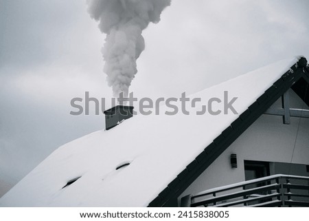 A cozy house in a snowy landscape emits smoke from its chimney as it heats up the interior while the exterior is covered in white snow.