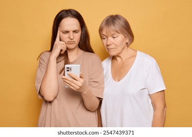 In a cozy indoor atmosphere, a younger woman appears troubled as she reads something on her smartphone, while an older woman observes closely, showing a look of worry. - Powered by Shutterstock