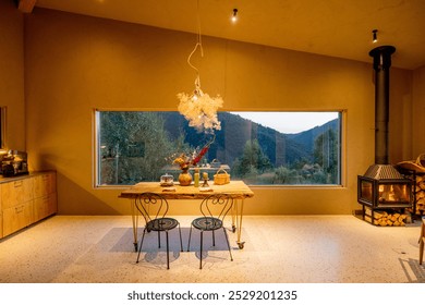 Cozy indoor space with a rustic table set against a large window with a view of the mountains during evening hours